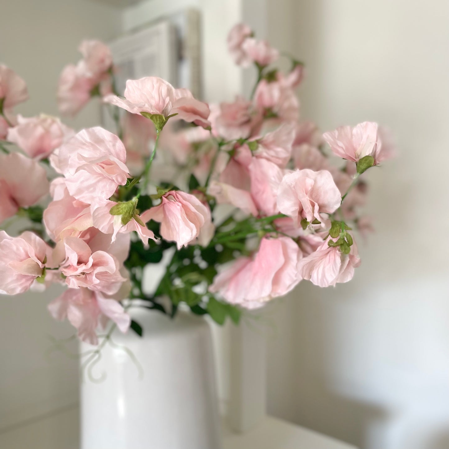 Pink faux sweet pea stems styled in a glass vase on a wooden table for a soft, elegant look.