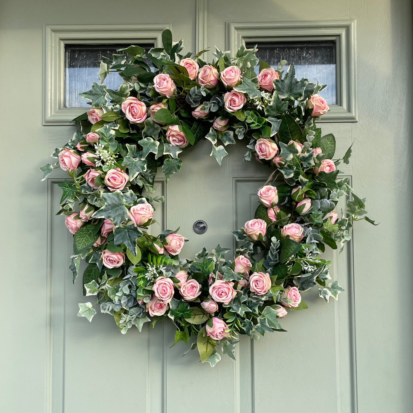 Summer faux wreath with pink roses, ivy and eucalyptus foliage styled on a rustic cottage green door.