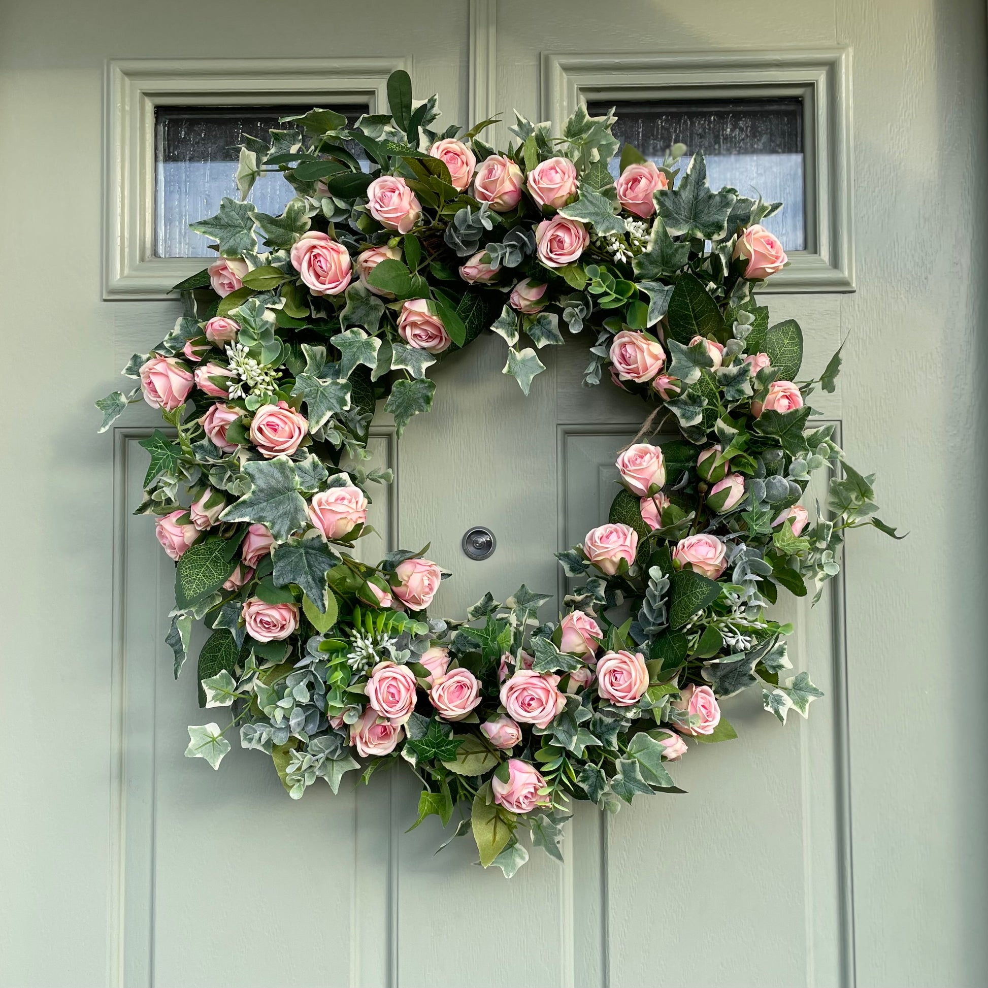 Summer faux wreath with pink roses, ivy and eucalyptus foliage styled on a rustic cottage green door.
