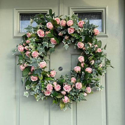 Summer faux wreath with pink roses, ivy and eucalyptus foliage styled on a rustic cottage green door.