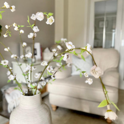 Faux white blossom spray with three stems styled in a stone vase in a neutral living room.