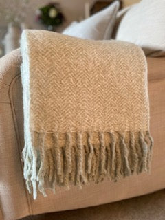Soft sage green herringbone mohair feel throw with fringed edges draped over a sofa, adding warmth and texture to a cosy living room.