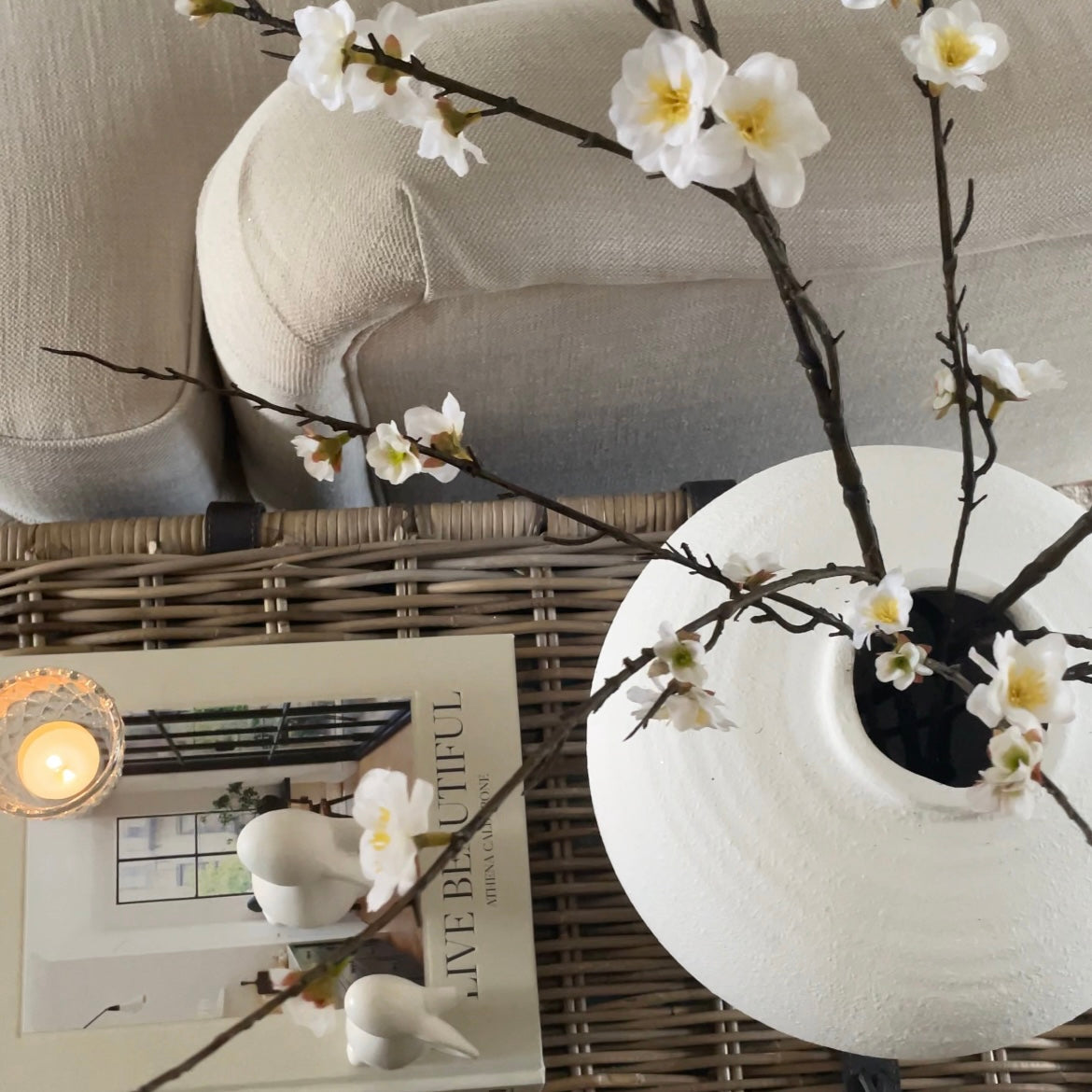 Two faux cherry blossom branches styled in Regola vase on a wicker coffee table.