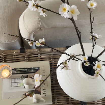 Two faux cherry blossom branches styled in Regola vase on a wicker coffee table.