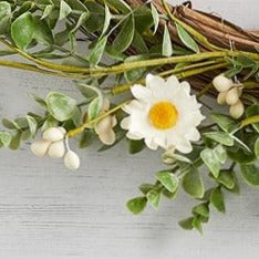 Close up of white daisies on greenery wreath. Styled on a white wooden background.