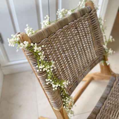 White faux gypsophila faux flower garland draped on a rattan chair.