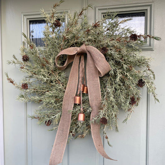 Rustic woodland Christmas wreath with jute bow and bronze metal cow bells. Styled on green cottage style door.