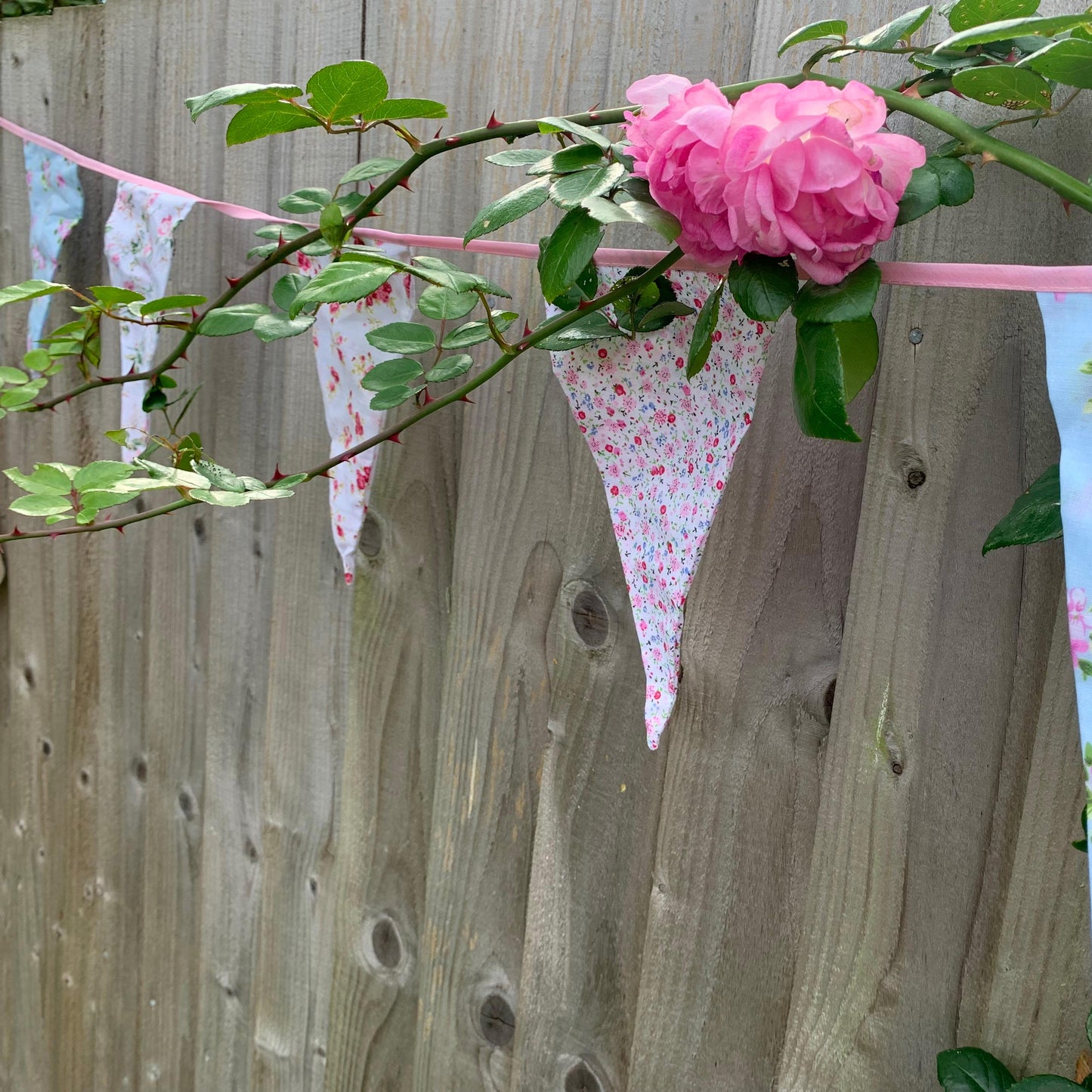 Floral material bunting with pink flowers against a wooden fence.