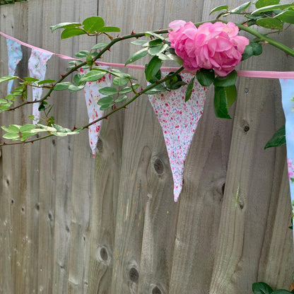 Floral material bunting with pink flowers against a wooden fence.