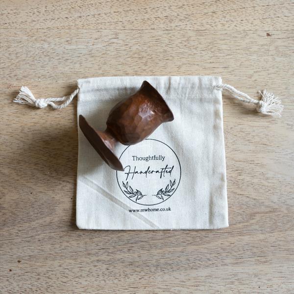 Gift ready forged candle holder with cotton presentation bag. Shown on a wooden table.