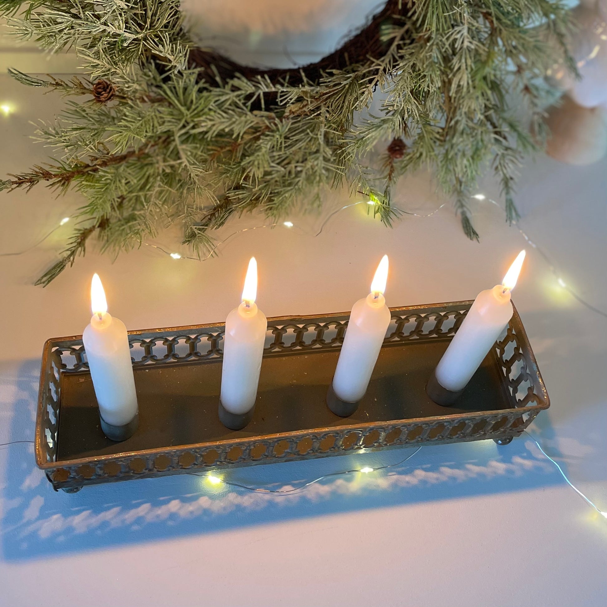 Nordic style candle holder creating warm winter glow. Styled on a white shelf with faux wreath.
