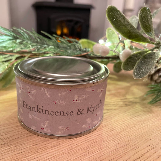 Frankincense and myrrh scented christmas scented candle in a tin with lid. Styled on a coffee table with a christmas garland.