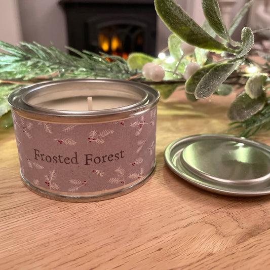 Frosted forest christmas scented candle in a tin. Styled on a wooden coffee table with a christmas garland.