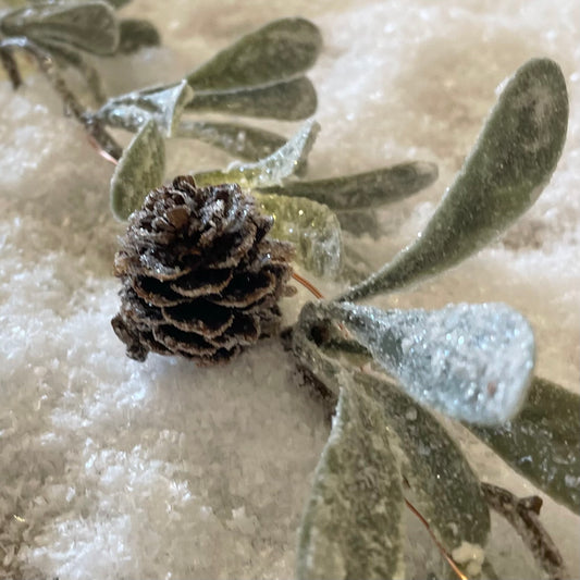 Winter garland with frosted miniature pinecones. Styled on a snowy background.