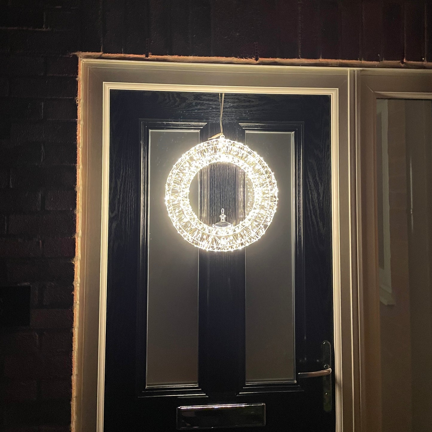Large LED wreath displayed outdoors with warm white lights. Shown on a back front door.