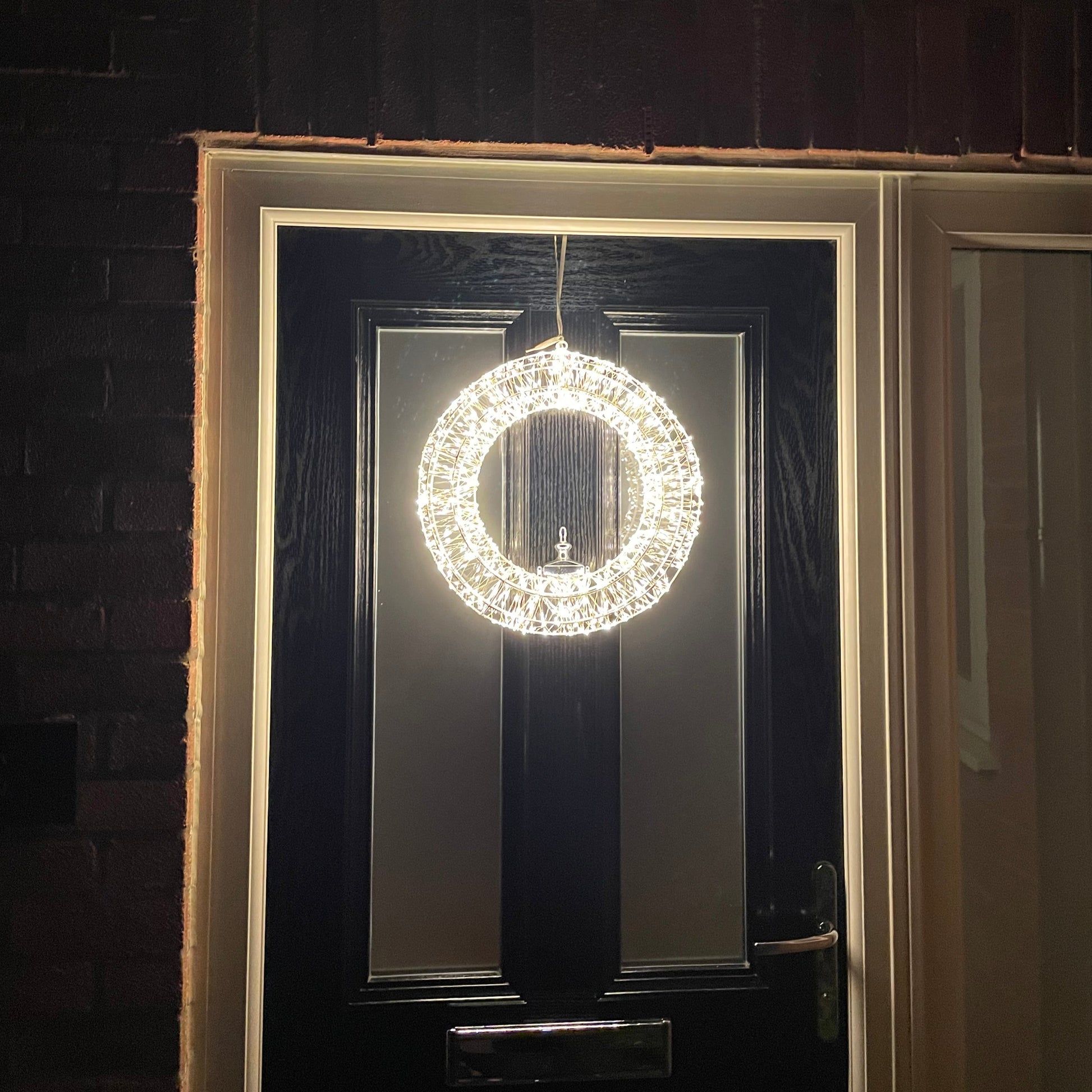 Large LED wreath displayed outdoors with warm white lights. Shown on a back front door.