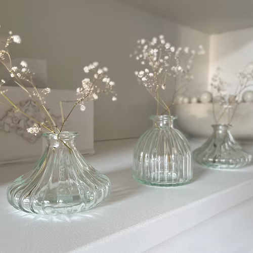 Three clear glass bud vases with decorative branches on a white surface.