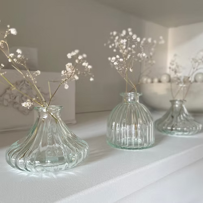Three clear glass bud vases with decorative branches on a white surface.
