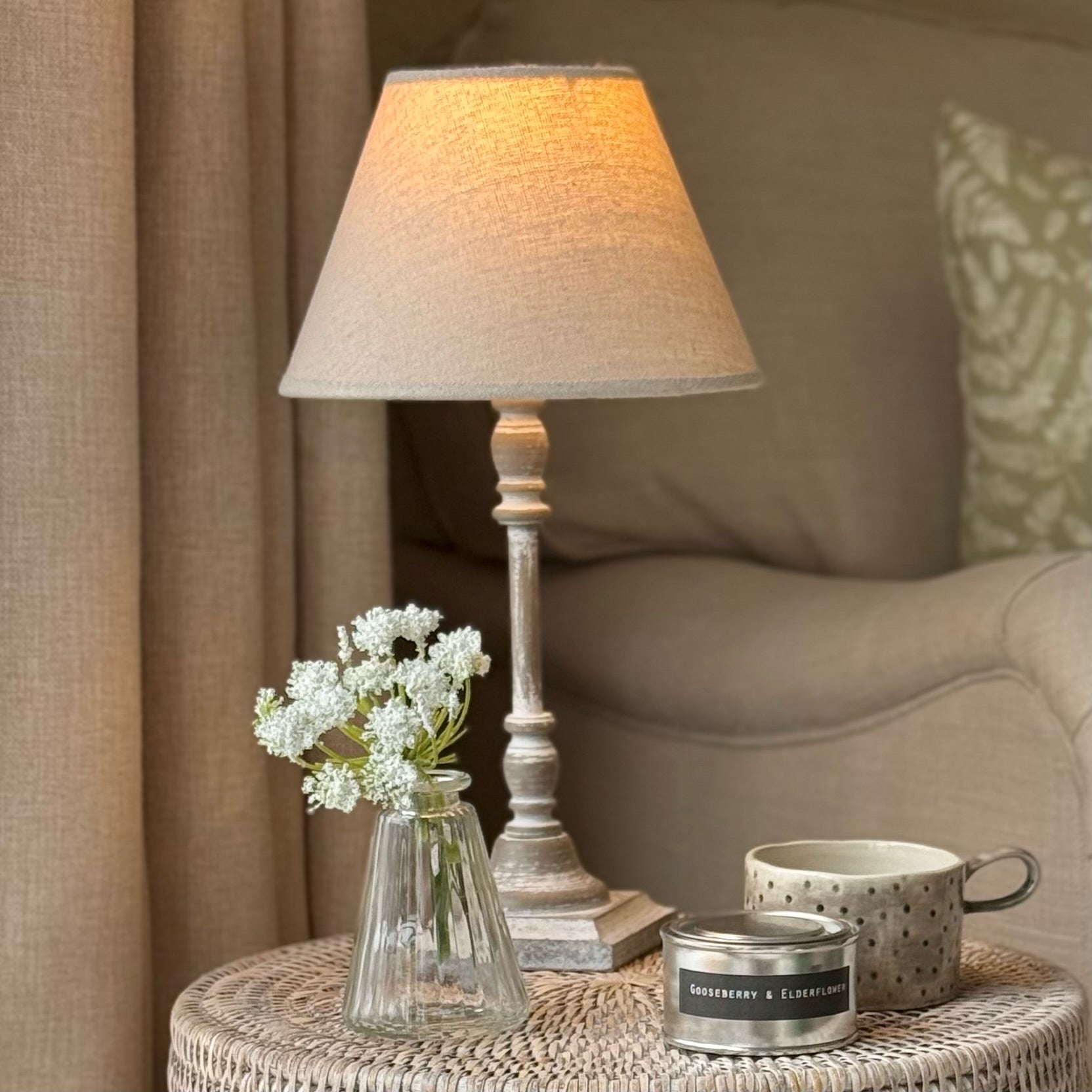 Lamp, vase with flowers, and mug on a table in a cozy living room setting.