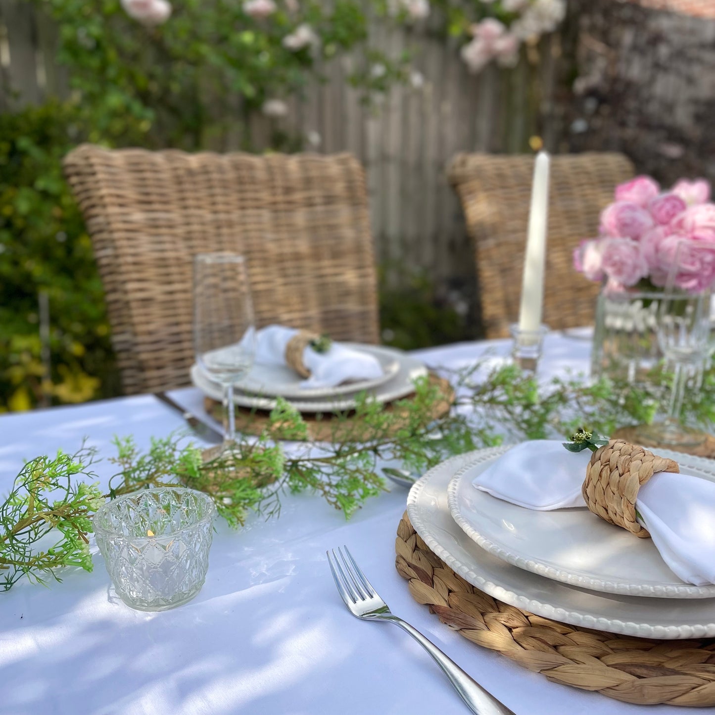 Clear glass tea light holder with an embossed diamond beaded pattern, styled on a table with soft, glowing candlelight. Shown on a garden table setting in a rose garden.