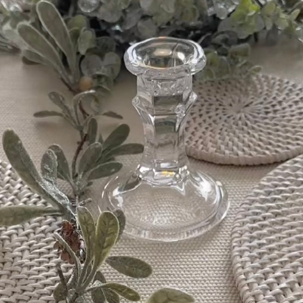 Elegant clear glass candlestick styled with a dinner candle on a rustic table setting. With garland and rattan coasters.