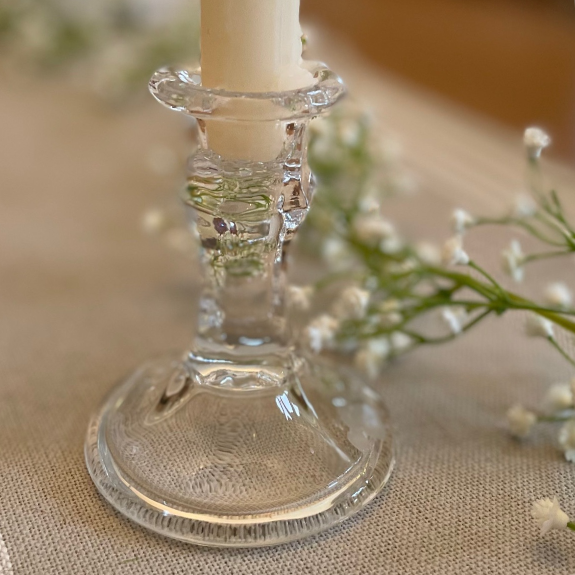 Elegant clear glass candlestick styled with a dinner candle on a rustic table setting.