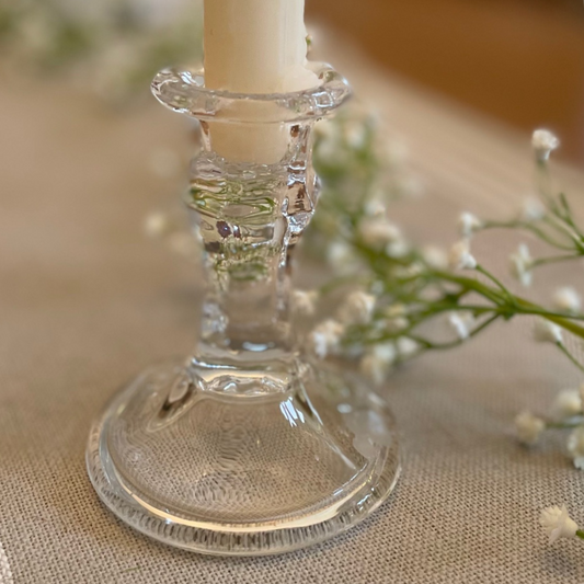 Elegant clear glass candlestick styled with a dinner candle on a rustic table setting.