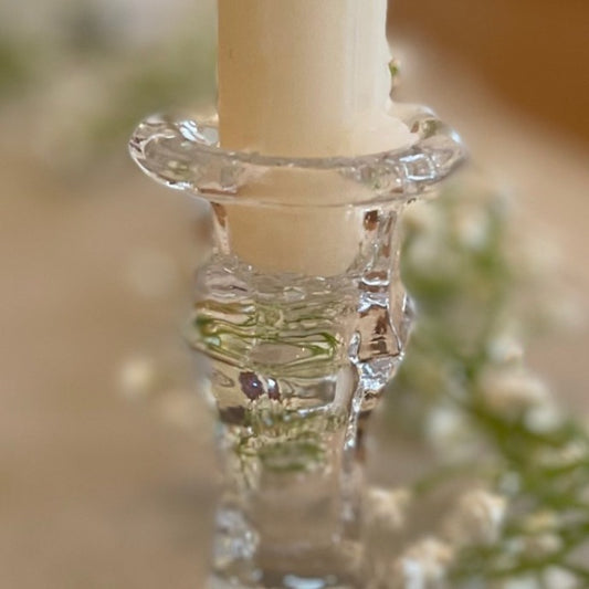Close up of elegant clear glass candlestick styled with a dinner candle on a rustic table setting.