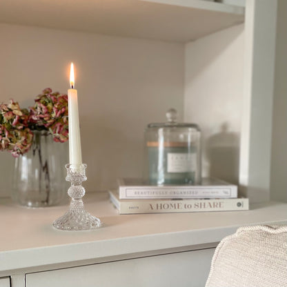 Clear glass cloche dome styled with a candle on a book and placed on a shelf with candle and vase of flowers.