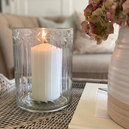 Glass hurricane lantern with leaf etched and ribbed glasswork. Styled on a rattan tray with flowers in a cosy living room