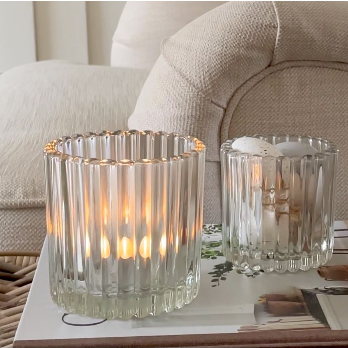 Two glass candle holders with lit candles on a table in a living room setting.