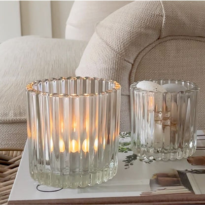 Two glass candle holders with lit candles on a table in a living room setting.