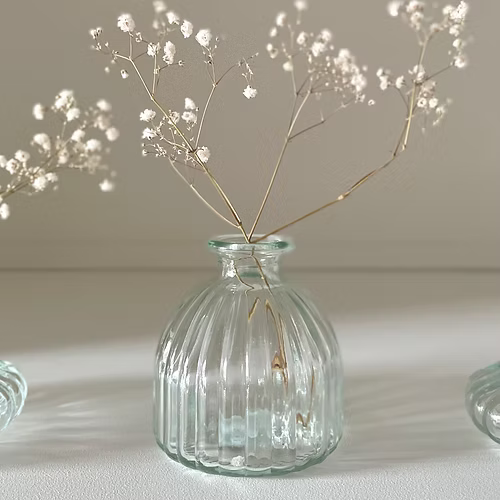 Clear glass bud vase styled with a single stem flower on a wooden table.