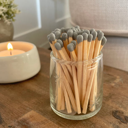 Glass match pot with etched star detail, grey matches and hidden striker pad on the base. Styled on a rustic wooden stool with candle.