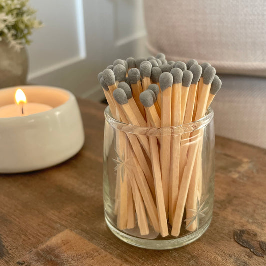 Glass match pot with etched star detail, grey matches and hidden striker pad on the base. Styled on a rustic wooden stool with candle.