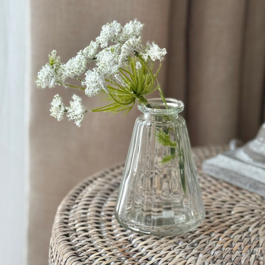 Tapered pyramid style glass bud vase holding a single stem, styled on a windowsill in a calm, neutral interior.