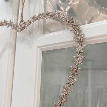 Heart shaped gold glitter star wreath hanging from natural jute string on a glass door.