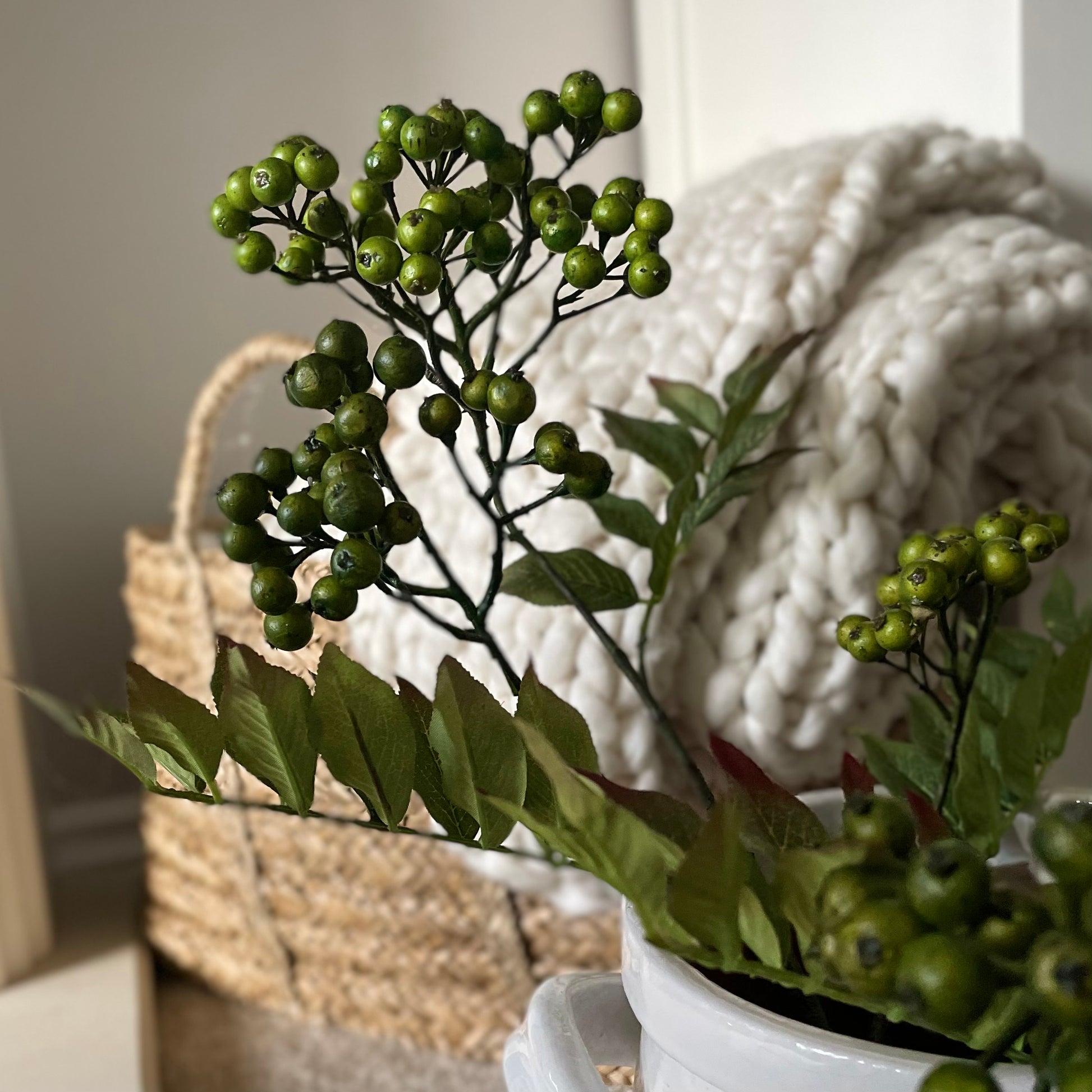 Close up of realistic artificial green berries on stem. Styled in a white vase in a cosy living room.