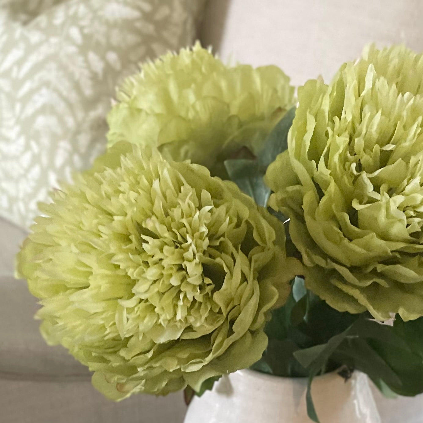 Close up of bright green peony bloom and lush foliage. Styled in a white ceramic short vase.