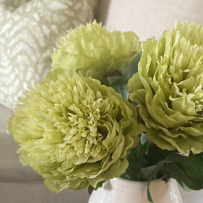 Close up of bright green peony bloom and lush foliage. Styled in a white ceramic short vase.