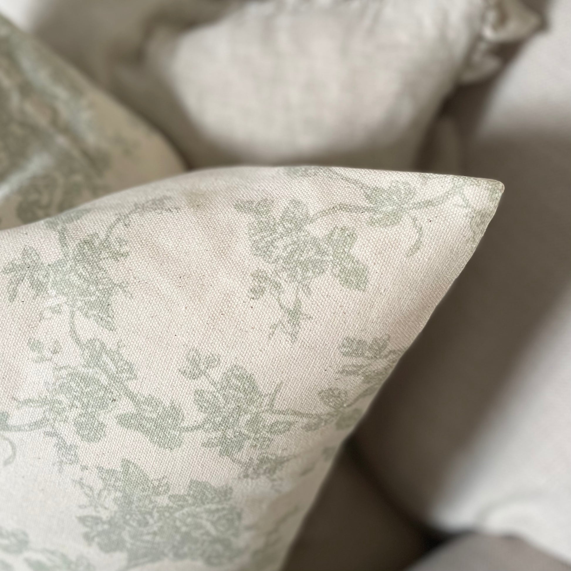 Sage green floral print cushion styled on a neutral linen sofa in a calm, country inspired living space.