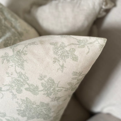 Sage green floral print cushion styled on a neutral linen sofa in a calm, country inspired living space.