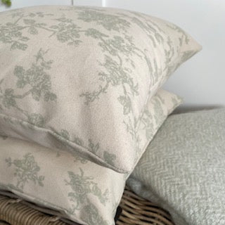 Sage green floral print cushion styled on a neutral linen sofa in a calm, country inspired living space.