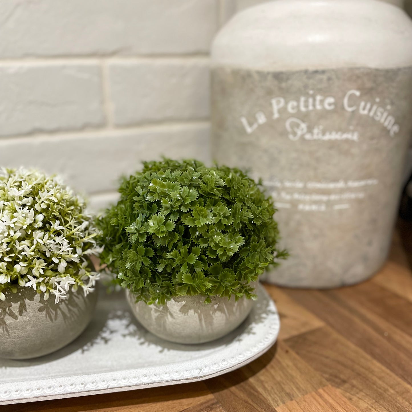 Faux green Hebe bush in a rustic cement pot styled on a wooden console table.