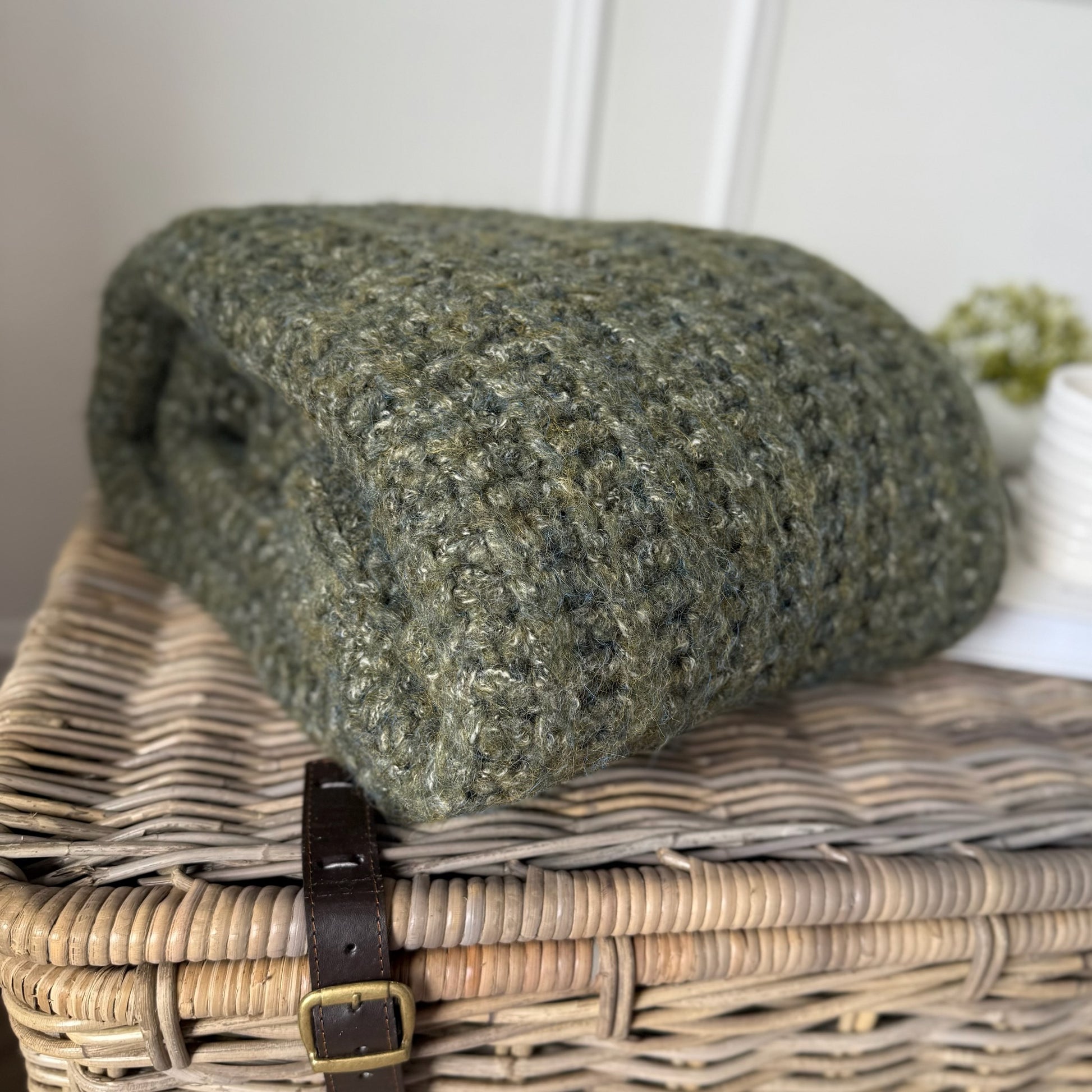 Green textured blanket on a wicker basket with a white background