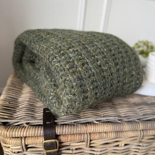 Green textured blanket on a wicker basket with a white background