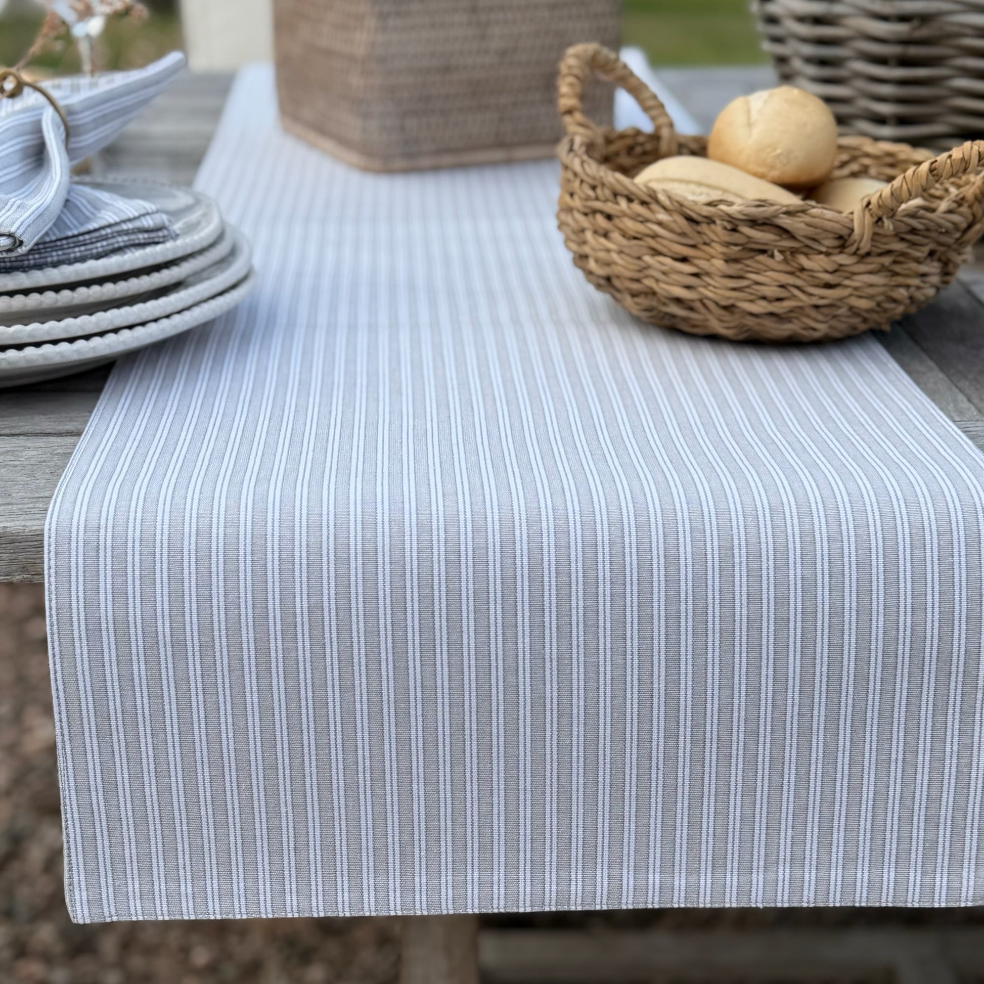 Table with a grey and white striped table runner, basket of bread and plates on a wooden table.