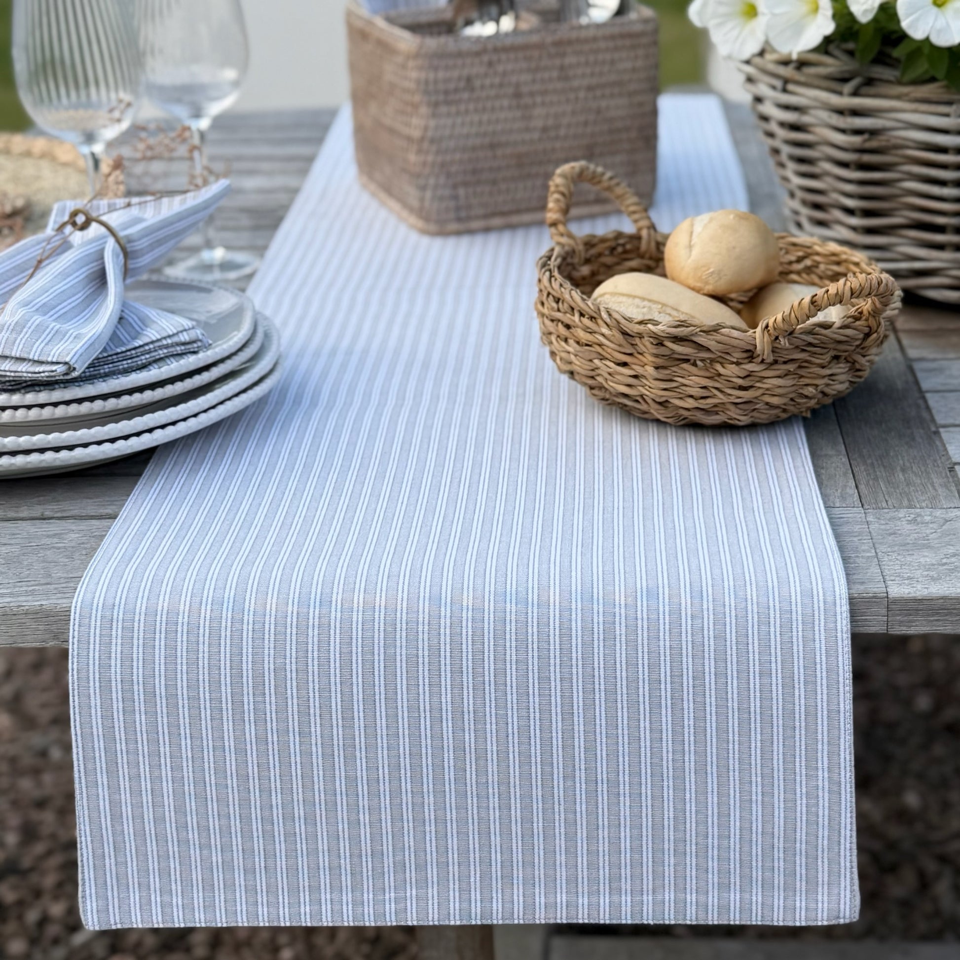 Dining table setting with a striped table runner, bread basket and plates.