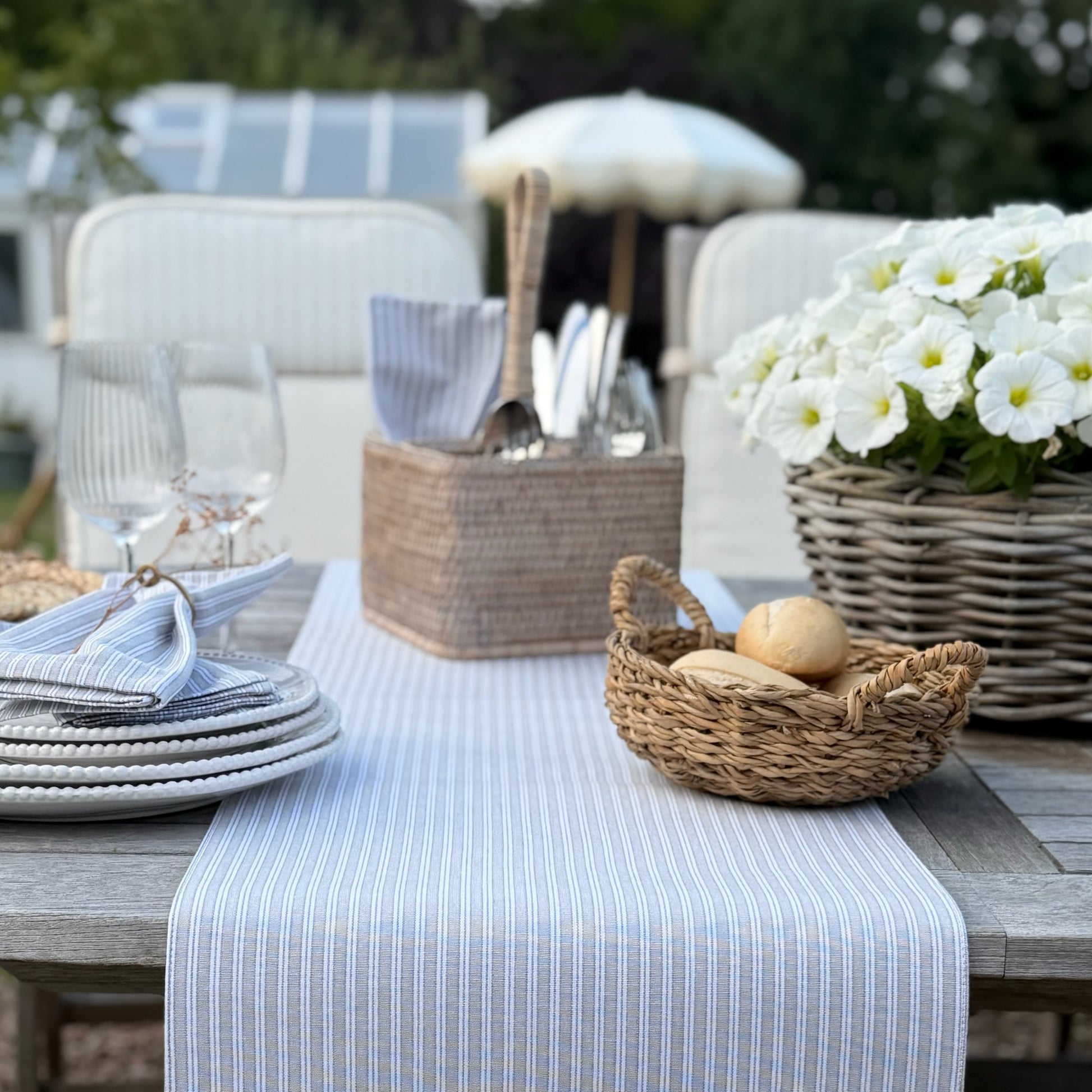Outdoor table setting with plates, cutlery, and bread on a striped table runner.