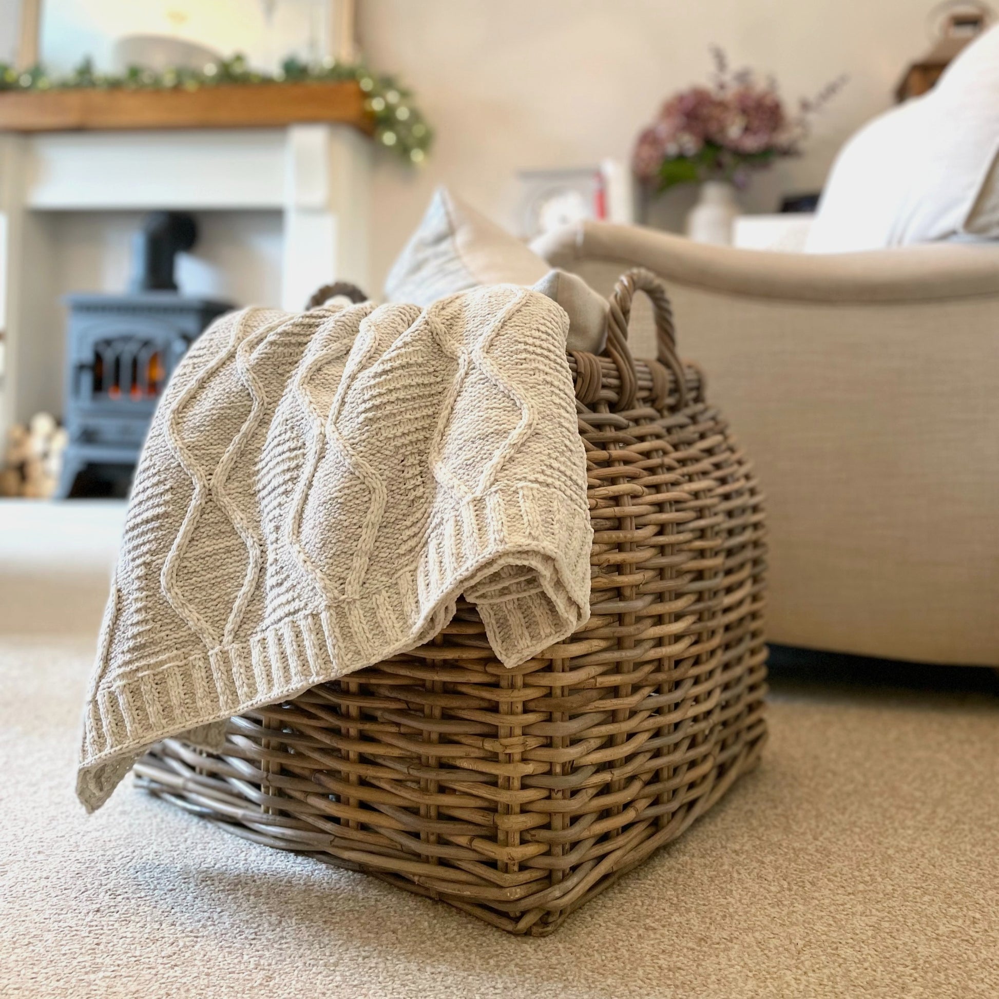 Soft melange grey chunky cable knit throw with ribbed edge draped over an armchair in a calm, cosy living room.